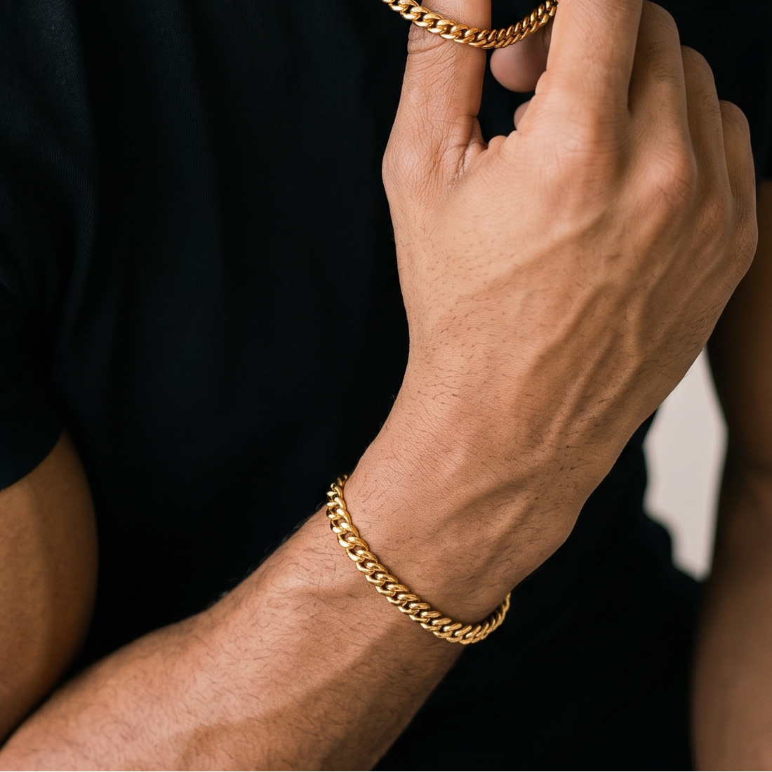 Man wearing a black t-shirt and gold chain necklace, adjusting the necklace.