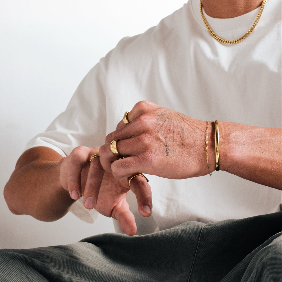 Men's Gold Drifter Cuff in 18k gold infused stainless steel, worn on his left wrist, seated, hands together