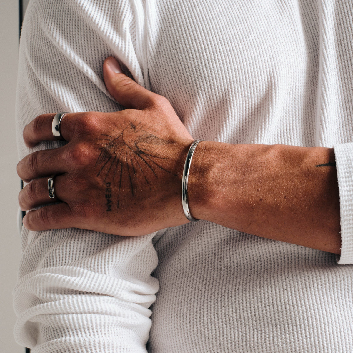 Men's Drifter Cuff in 316L stainless steel, silver finish, worn on his left wrist, hand gripping his other arm