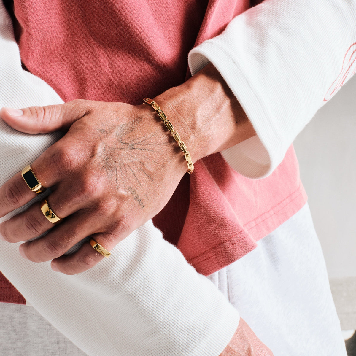Man wearing gold stainless rings, close up, hand over his forearm, with a gold box link chain bracelet