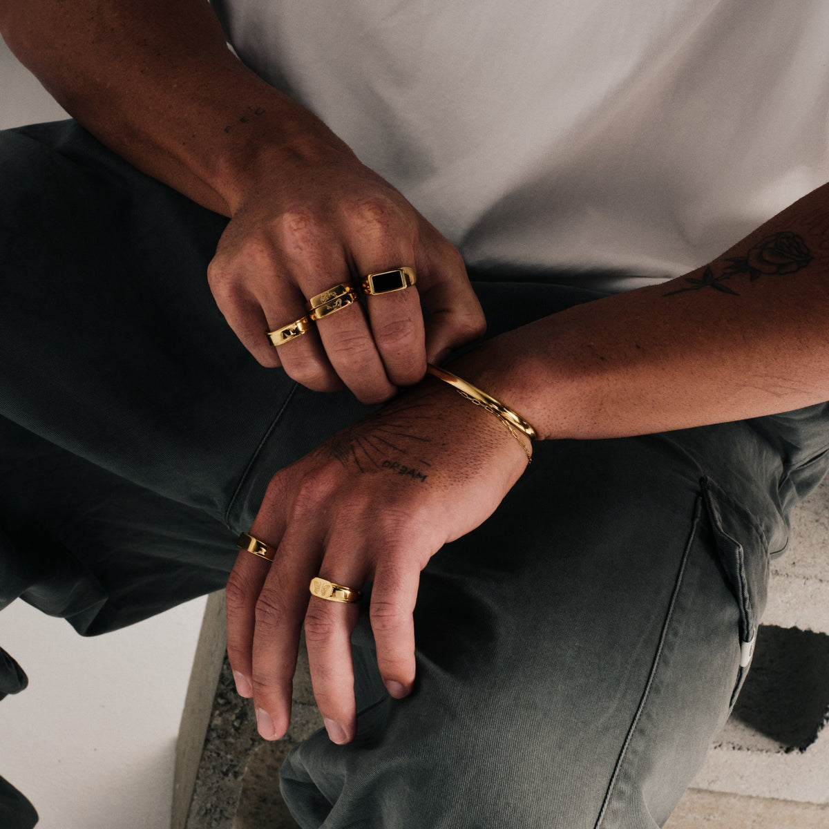 Men's Gold Koi Stackers in 18k gold infused stainless steel, both worn on his right middle finger, white tee, olive pants