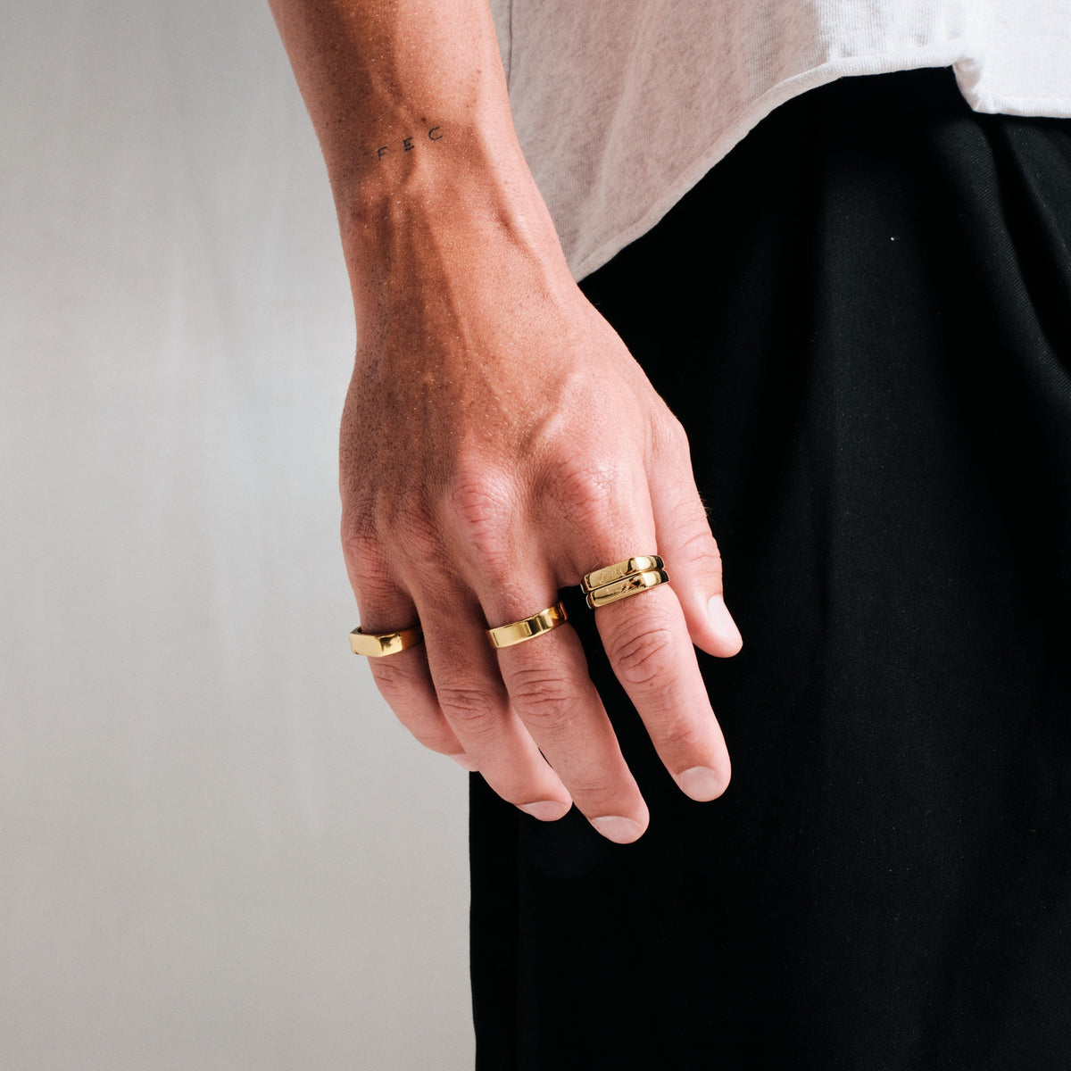 Men's Gold Koi Stackers in 18k gold infused stainless steel, both worn on his right index finger, hand relaxed at his side