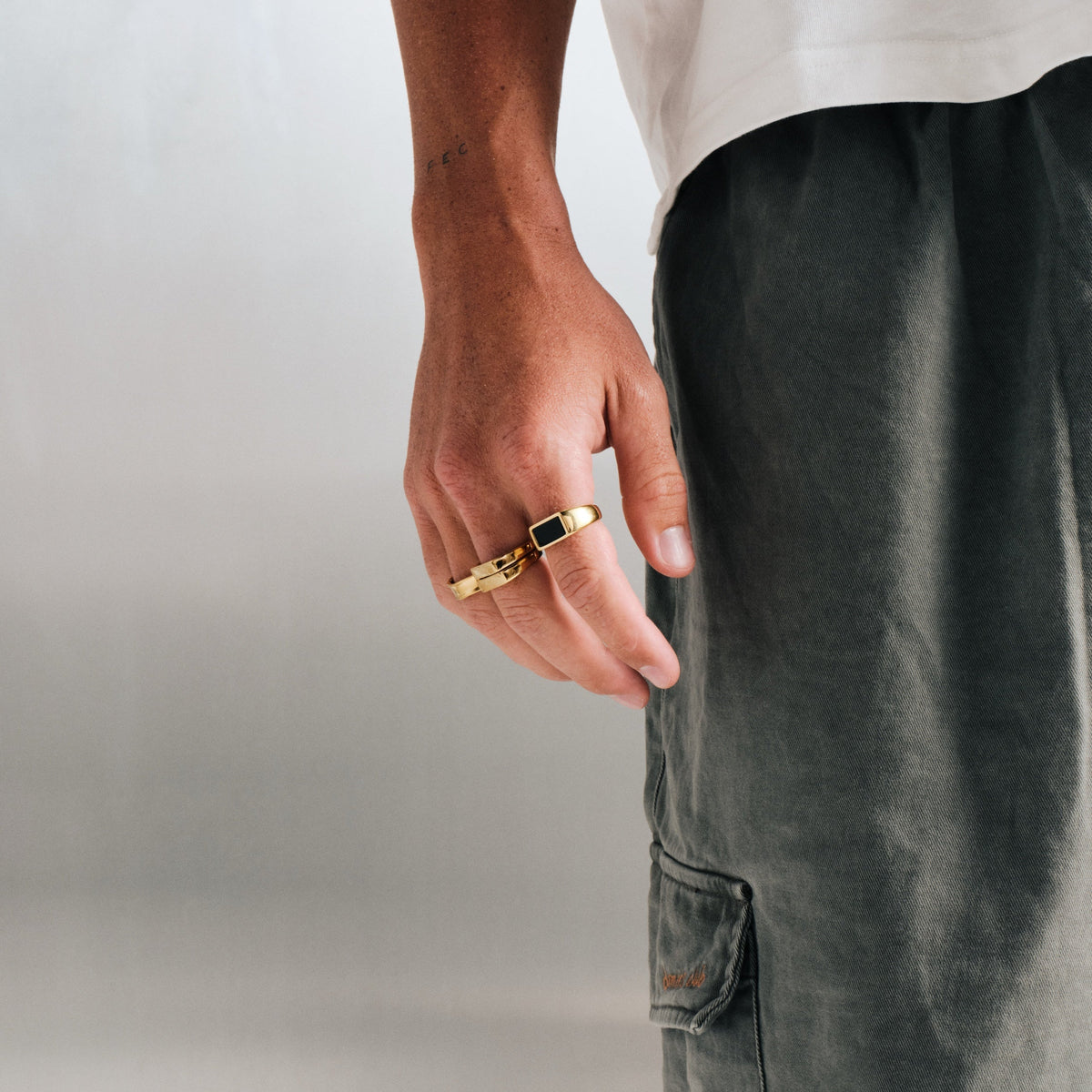 Men's Gold Koi Stackers in 18k gold infused stainless steel, both worn on the middle finger, hand relaxed at his side
