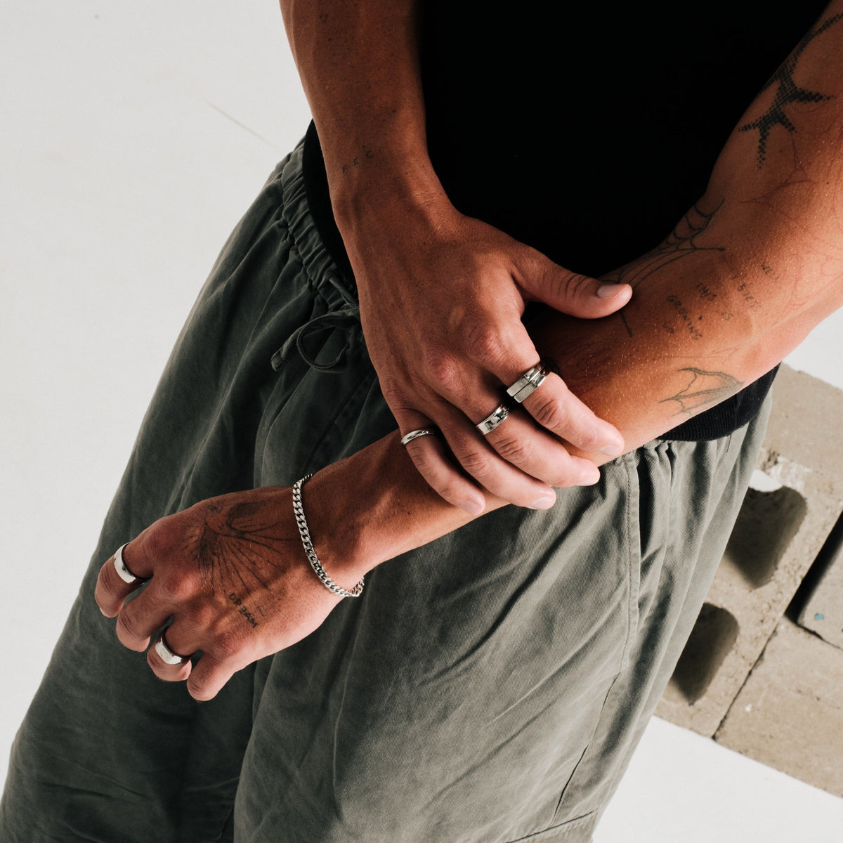 Men's Koi Stackers in 316L stainless steel, silver finish, both worn on the index finger, arms crossed, hand gripping forearm