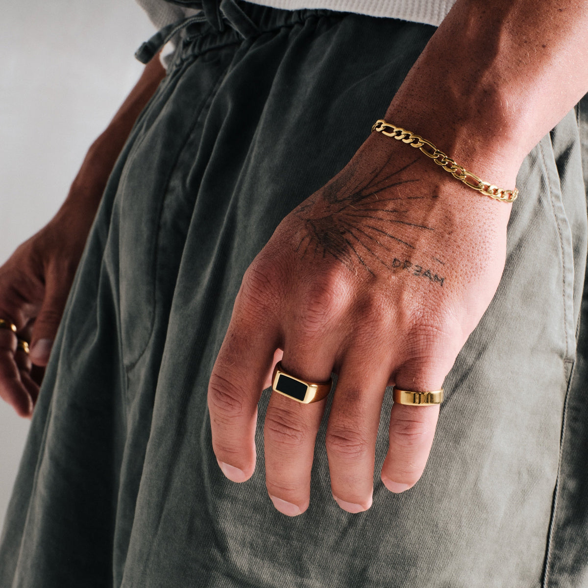 Men's Gold Onyx Ring in 18k gold infused stainless steel, worn on his left middle finger, hand by his side, olive pants
