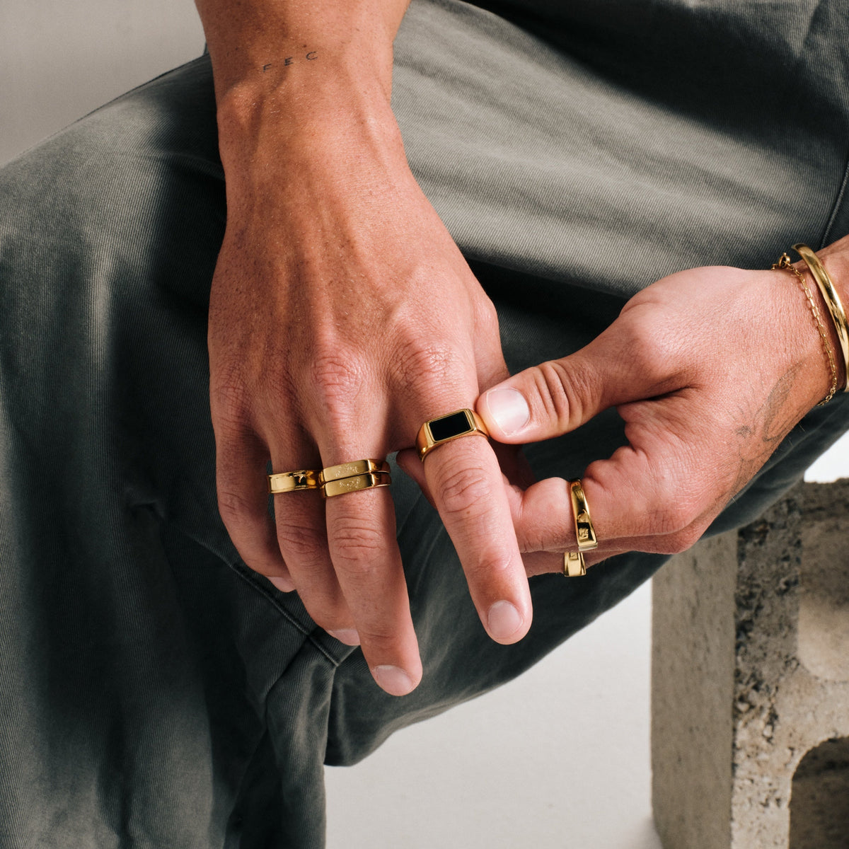 Men's Gold Onyx Ring in 18k gold infused stainless steel, worn on his right index finger, olive pants