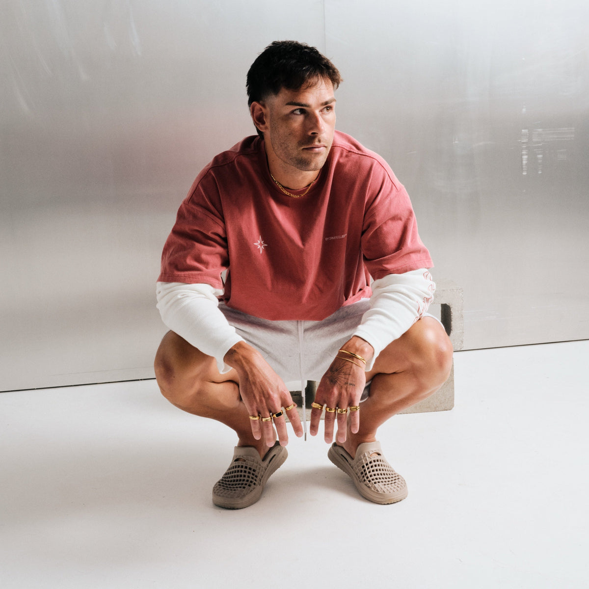 Man wearing gold stainless rings, crouching, with a gold chain necklace, gold bracelets