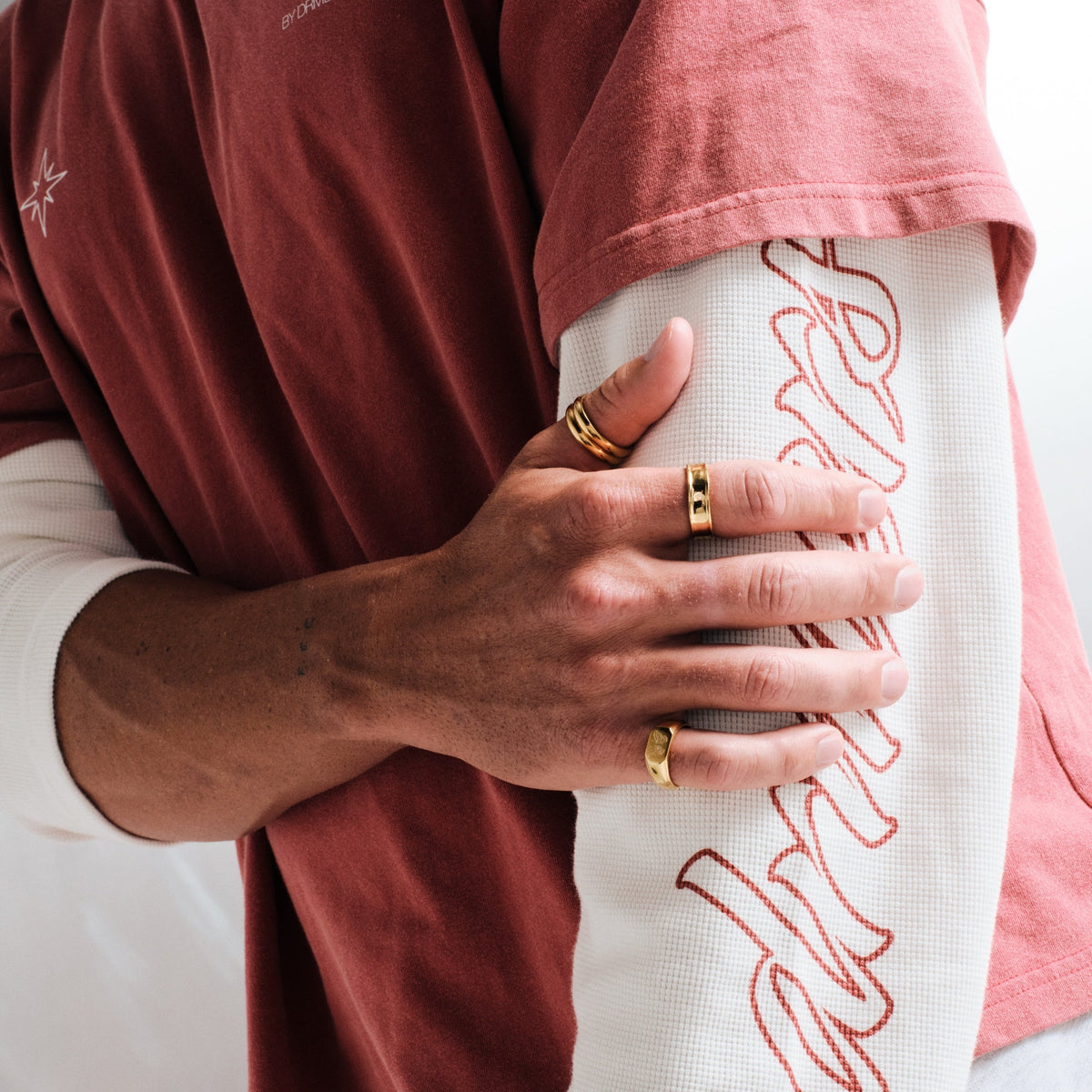 Men's Gold Revival Ring in 18k gold infused stainless steel, worn on the little finger, hand gripping his other arm