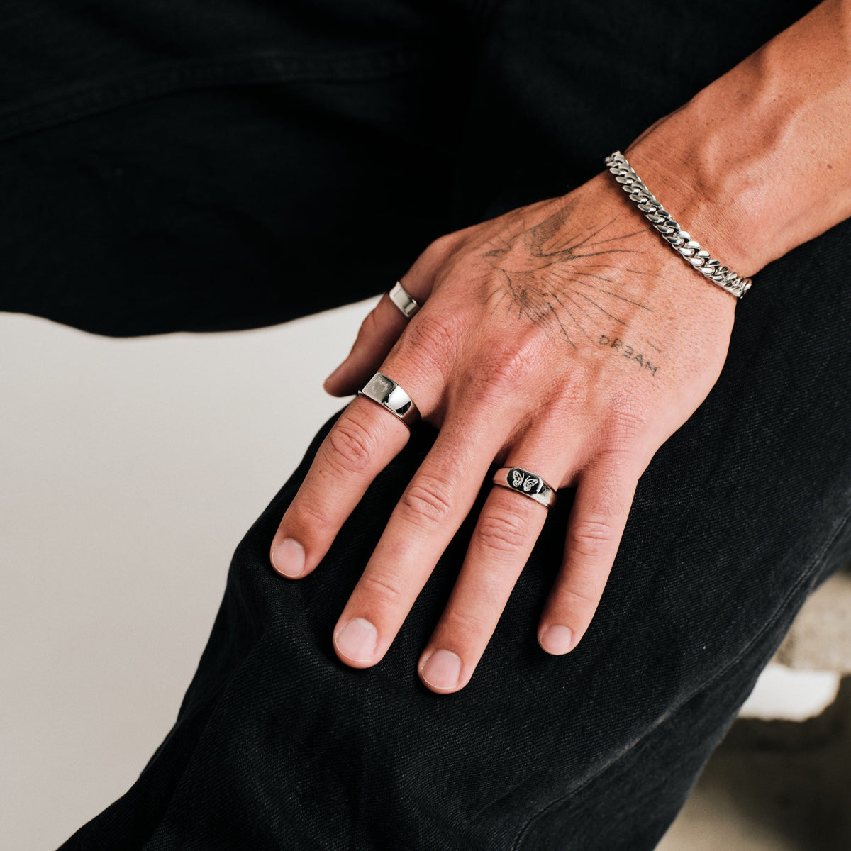 Men's Revival Ring in 316L stainless steel, silver finish, worn on his left ring finger, hand resting on knee, black jeans