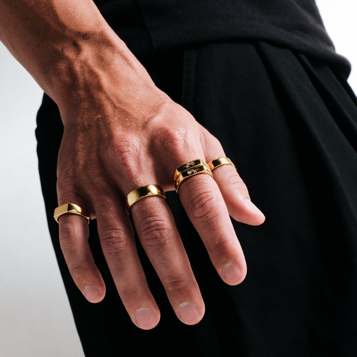 Men's Gold Rosa Stackers in 18k gold infused stainless steel, in a stack, hand hanging by his side, black tee, black pants