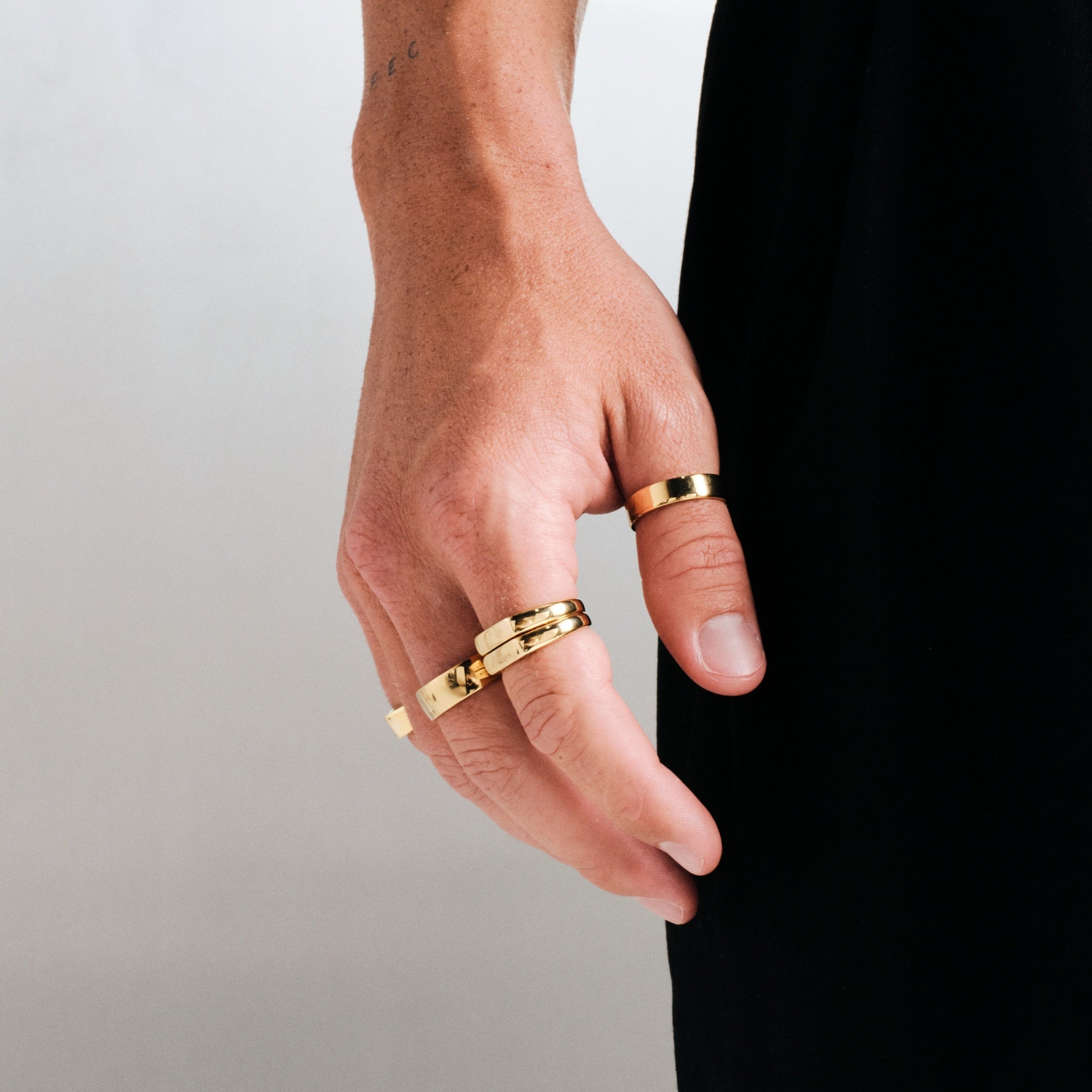 Men's Gold Serenity Ring in 18k gold infused stainless steel, worn on the thumb, hand hanging by his side, black pants