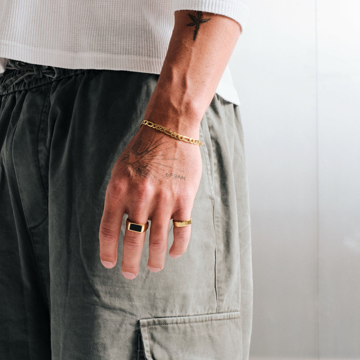 Man wearing gold stainless rings, hand by his side, with a gold Figaro bracelet on left wrist