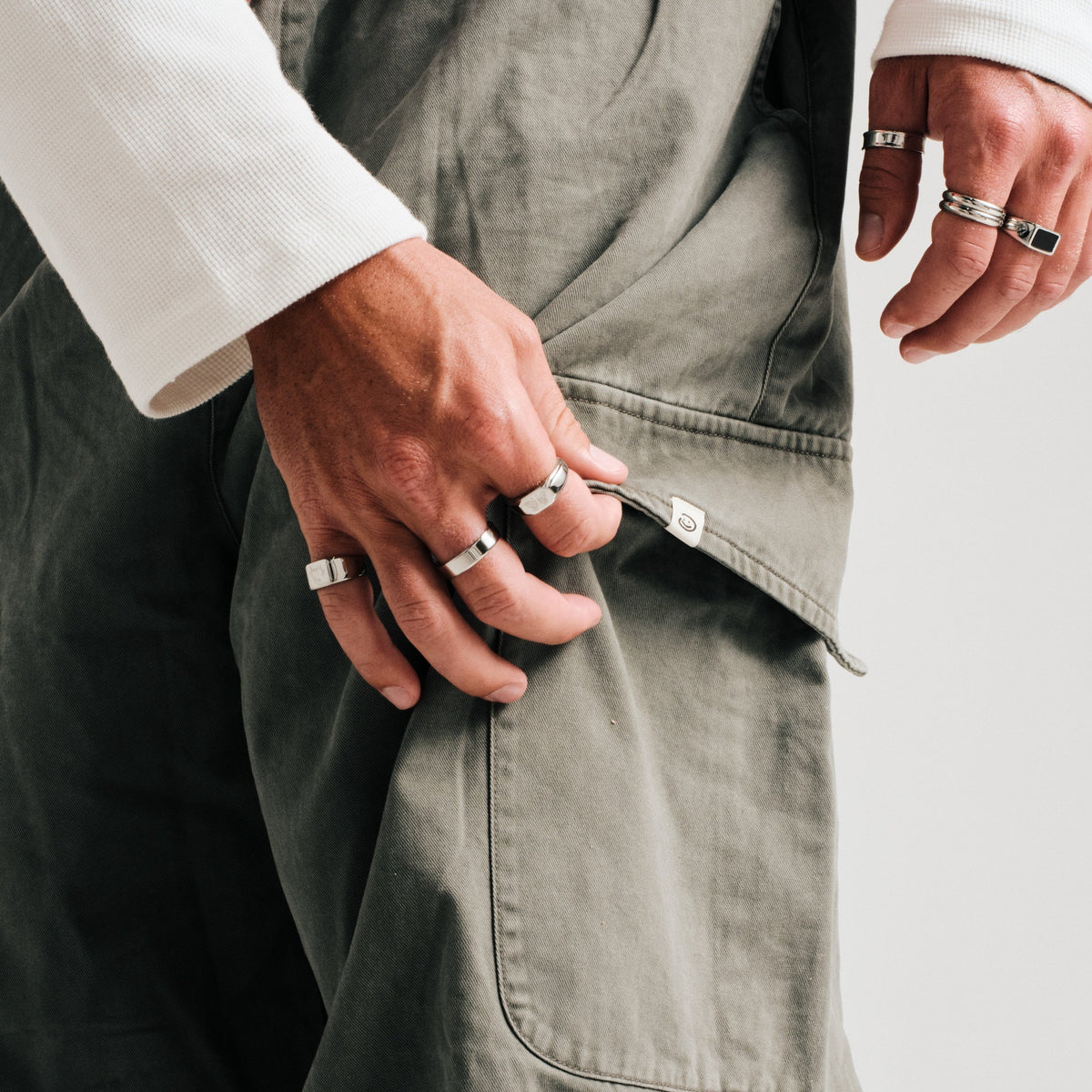 Men's Serenity Ring in 316L stainless steel, silver finish, worn on the middle finger, hand tugging his cargo pocket
