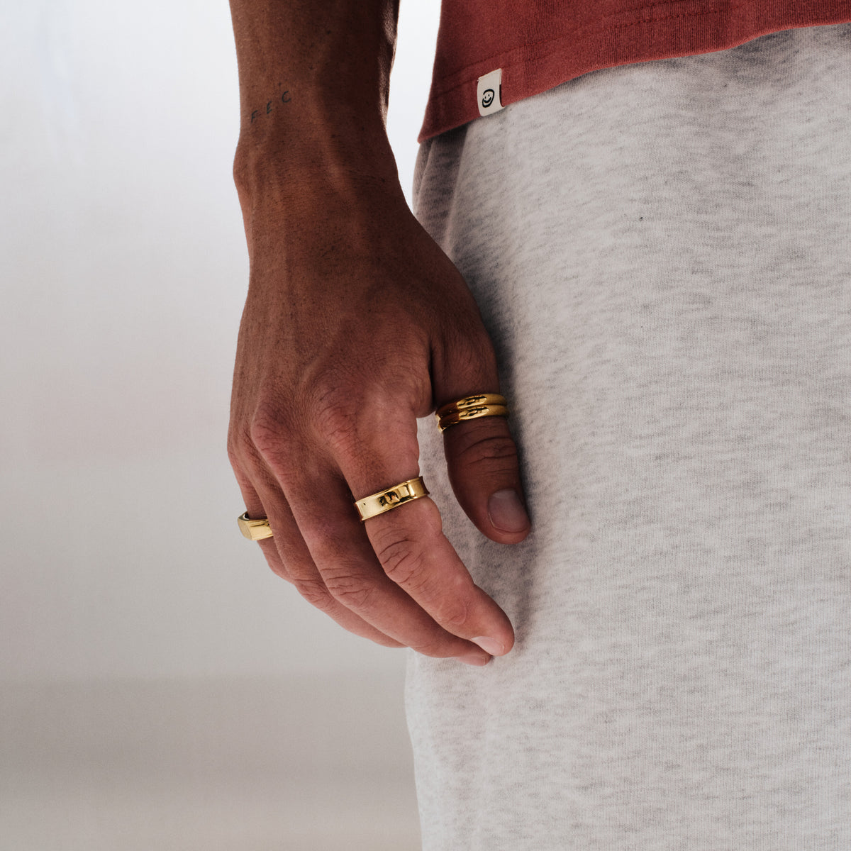 Men's Gold Stacker Rings in 18k gold infused stainless steel, both worn on his right index finger, hand relaxed at his side