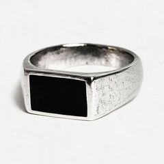 A silver signet ring with a textured band and a rectangular black inlay, photographed on a clean white background.
