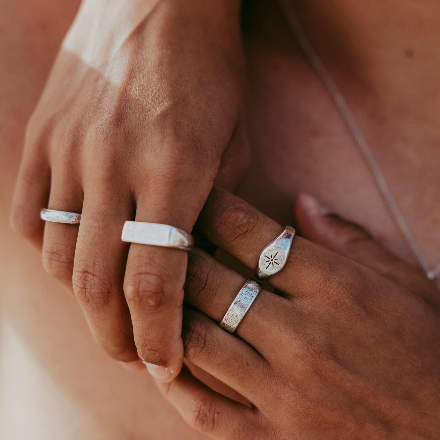 Two hands clasped together, showcasing a collection of Billie Jo silver rings including the Luminous Ring. A modern, masculine jewellery aesthetic.