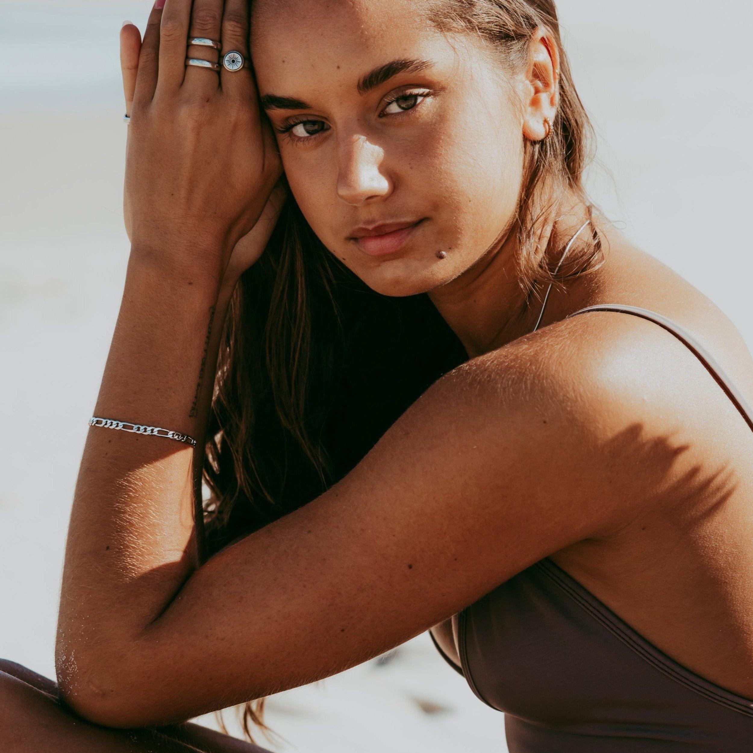 A woman wearing the Billie Jo Oracle Ring on her index finger, her hand resting gently on her forehead. This editorial shot captures a serene, beachy vibe, showcasing the versatility of this sterling silver men\s ring.