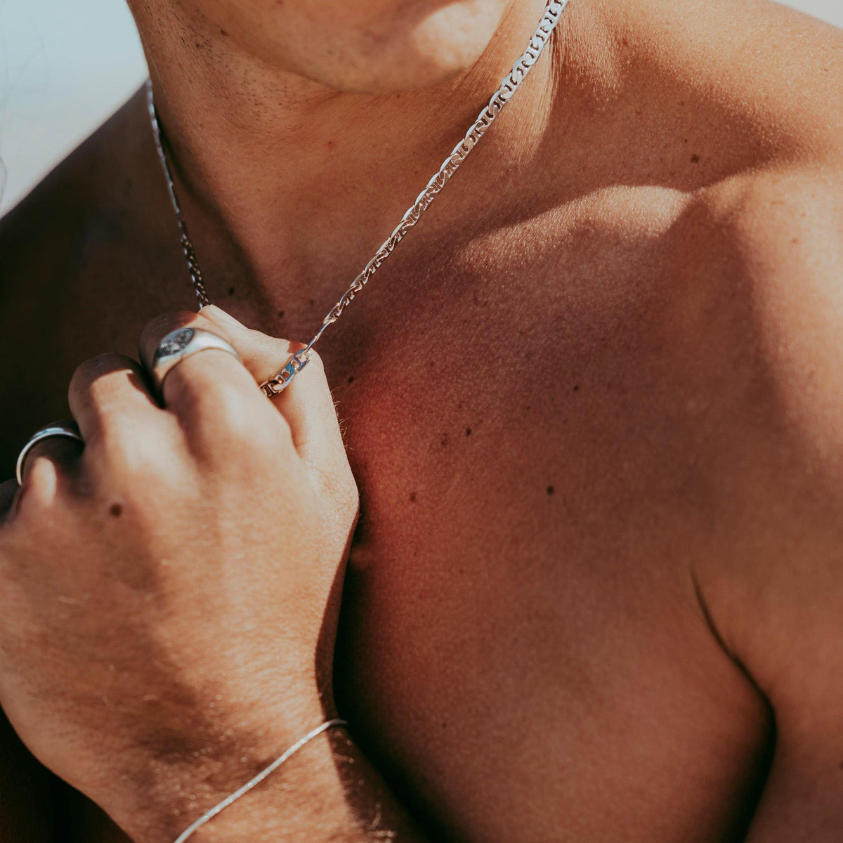 A detailed close-up shot of a man\'s hand adjusting the sterling silver Mariner Necklace from Billie Jo, highlighting the chain\'s texture.